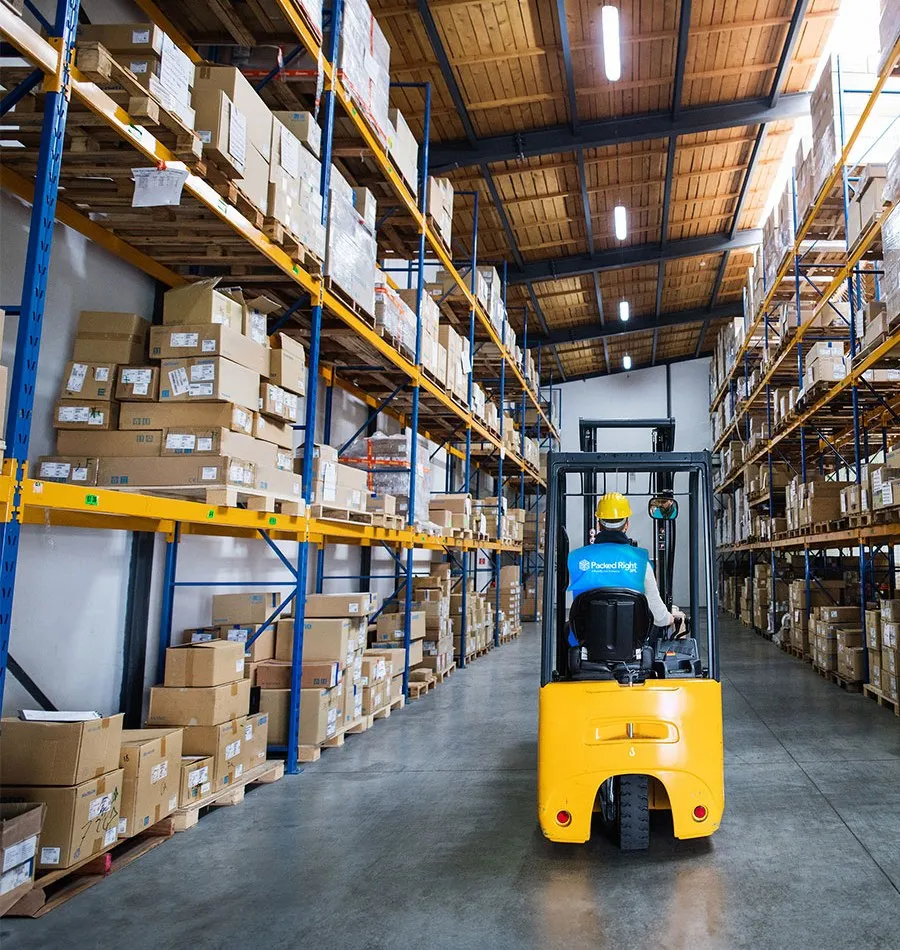 Packed Right forklift operator driving down a warehouse aisle